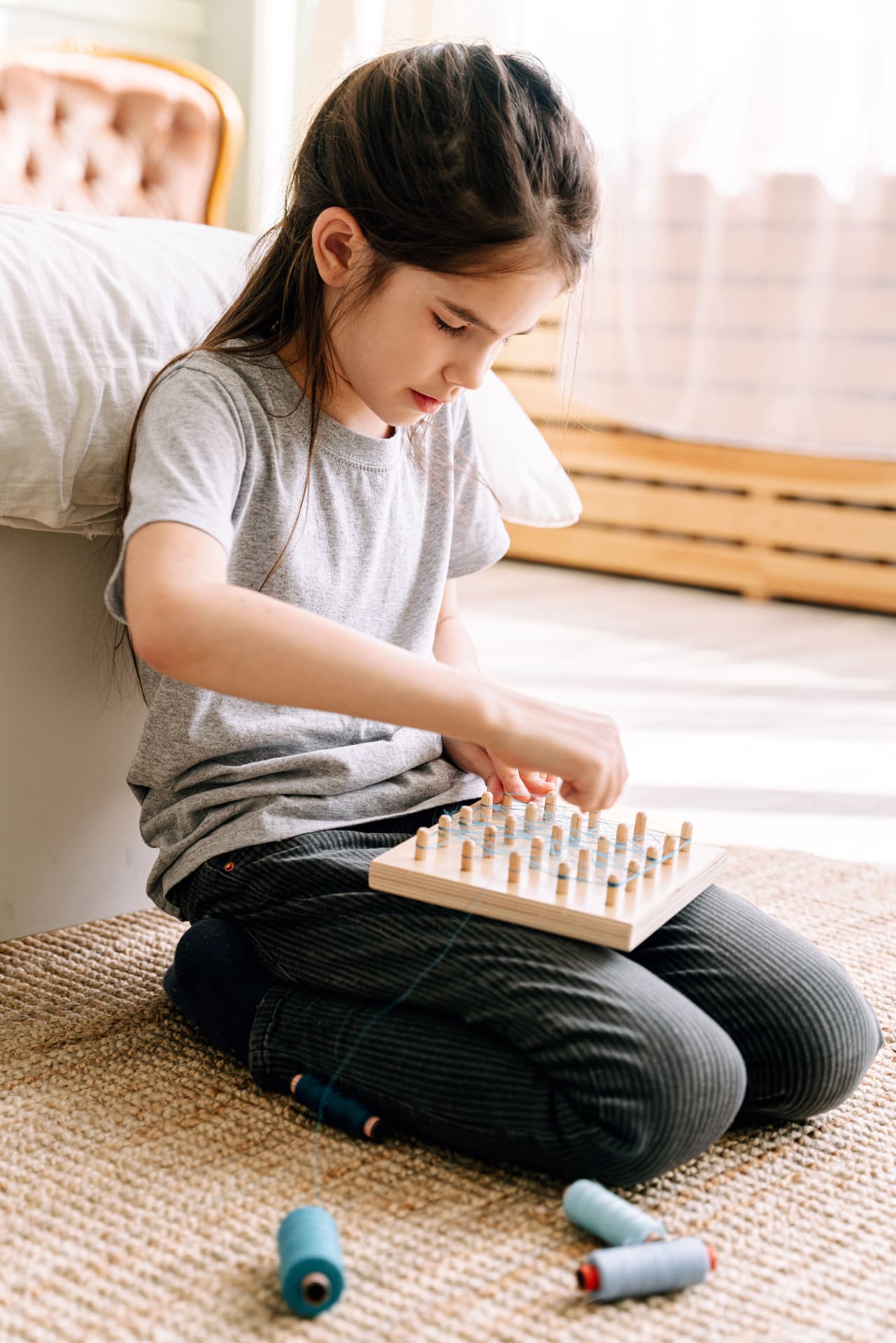 Child threading elastics on a wooden pegboard to build fine motor skills